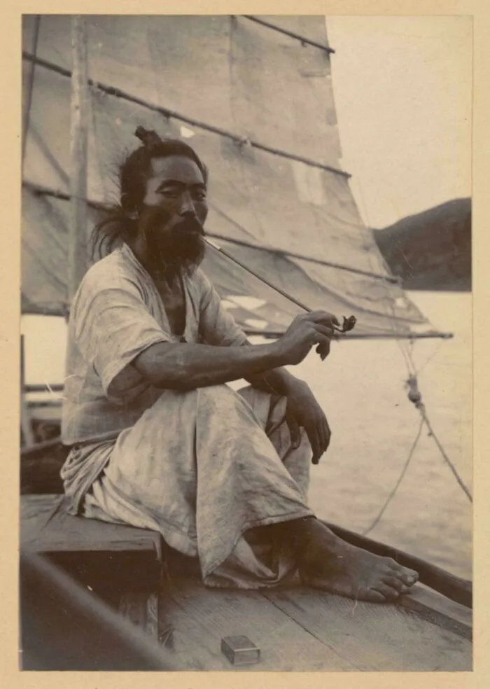 Korean sailor resting on a boat, smoking a bamboo pipe, circa 1904 | korean sailor photo
